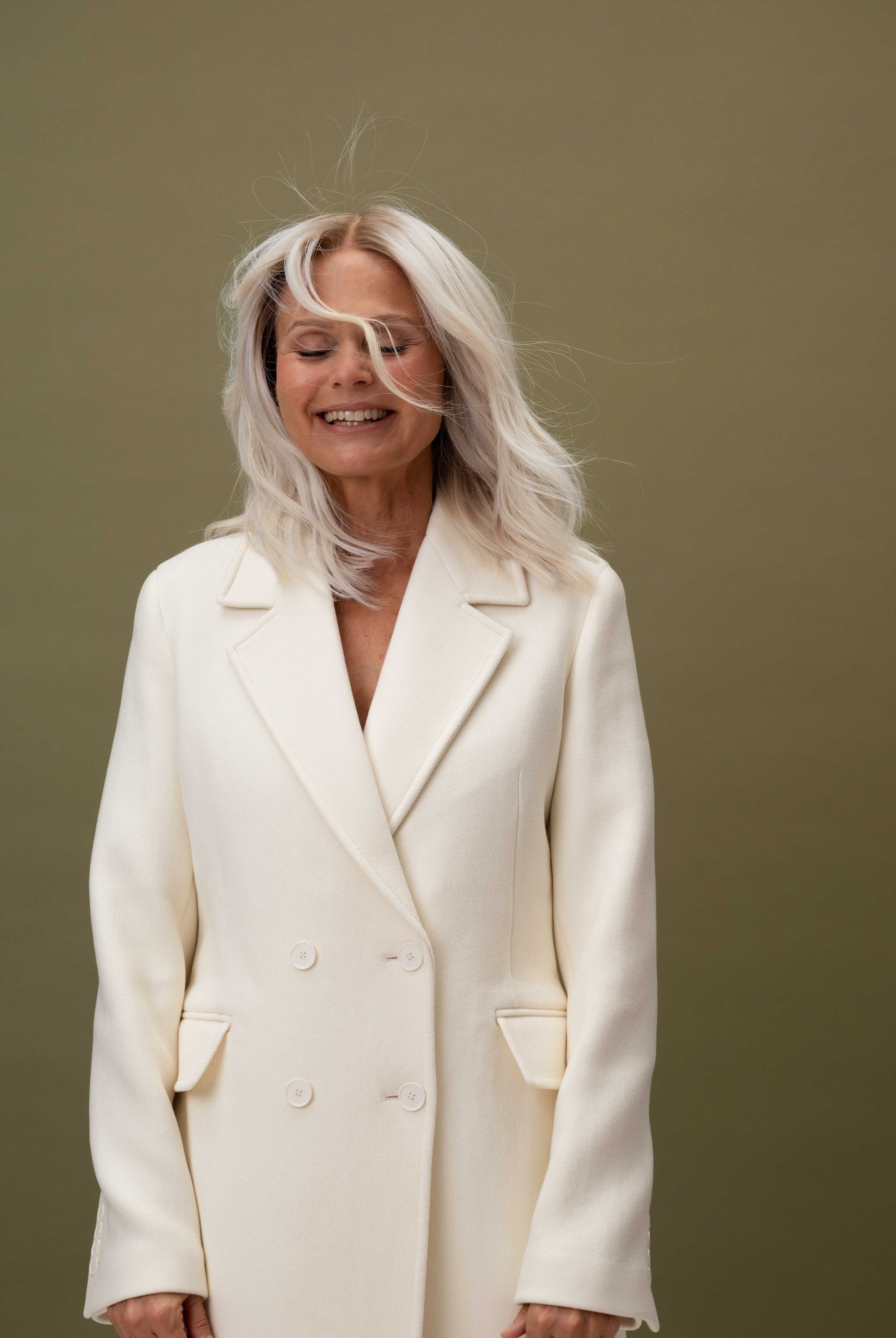 Fiorella Wig 35 cm platinum ash blonde Remy human hair wig with darker root and light waves, worn by model in white blazer.