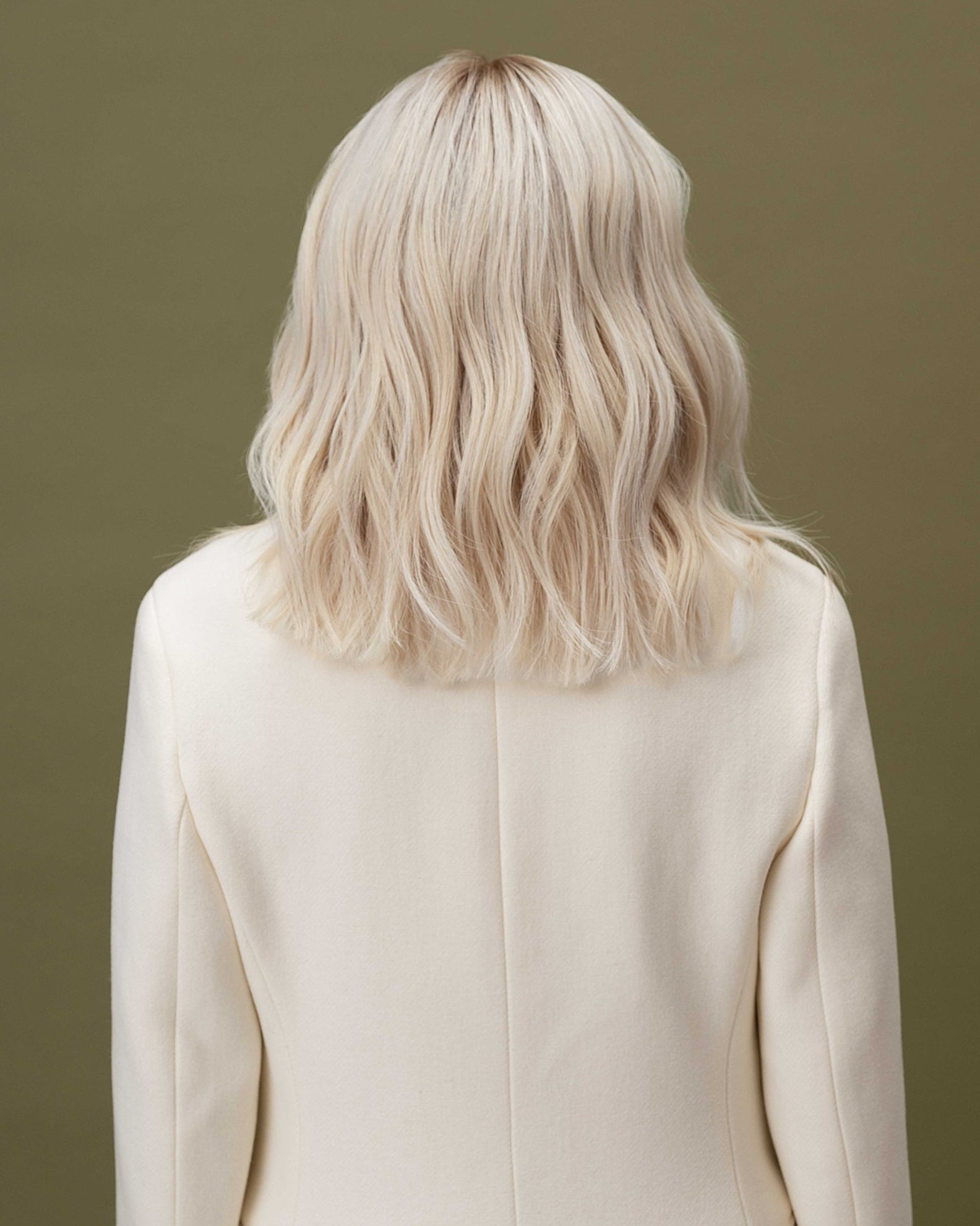 Fiorella Wig 35 cm human hair wig in platinum ash blonde with natural darker root, softly layered and shown from the back on model.