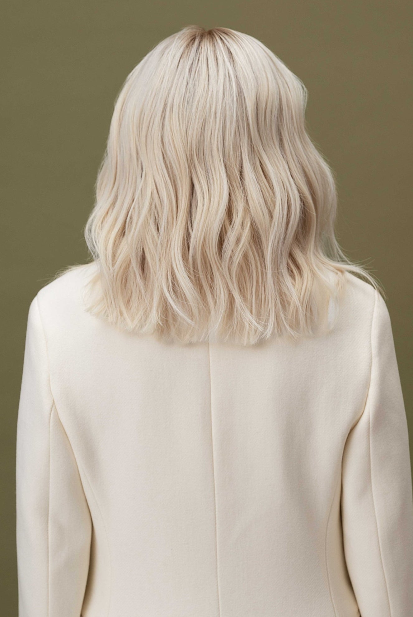 Fiorella Wig 35 cm human hair wig in platinum ash blonde with natural darker root, softly layered and shown from the back on model.