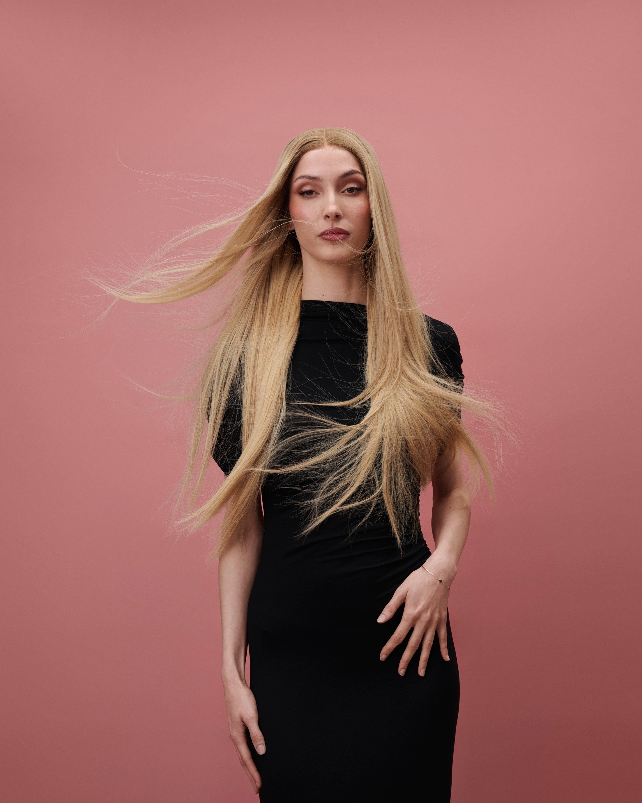 Vera Wig / 65cm – 65 cm light blonde Remy human hair wig with golden undertones and darker roots, displayed on a model facing forward against a pink background.