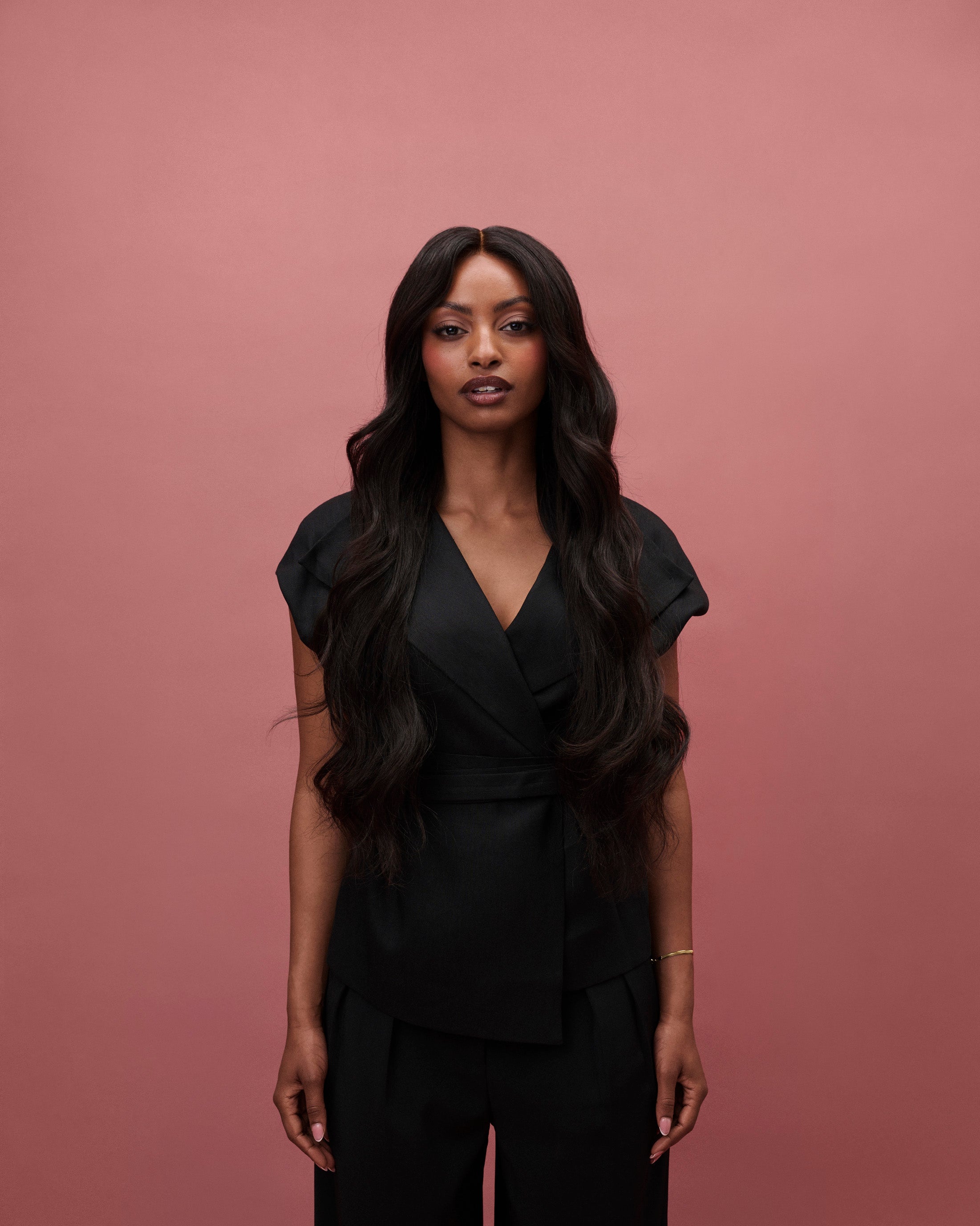 Aurora Wavy Wig 65 cm – dark brown Remy human hair wig with soft beach waves on HD lace, worn by a model in a black outfit against a pink background