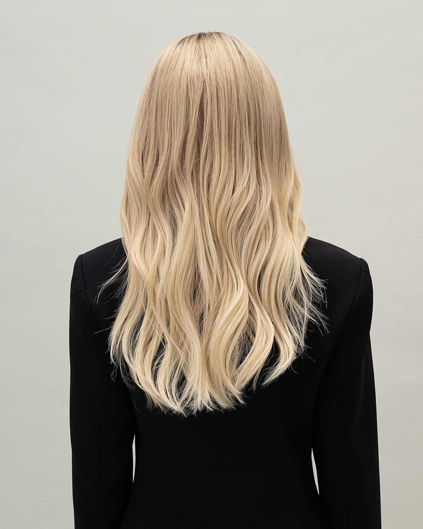 Vera Wig 40 cm light blonde human hair wig with natural darker roots, softly layered cut for volume and movement, shown from the back on model.