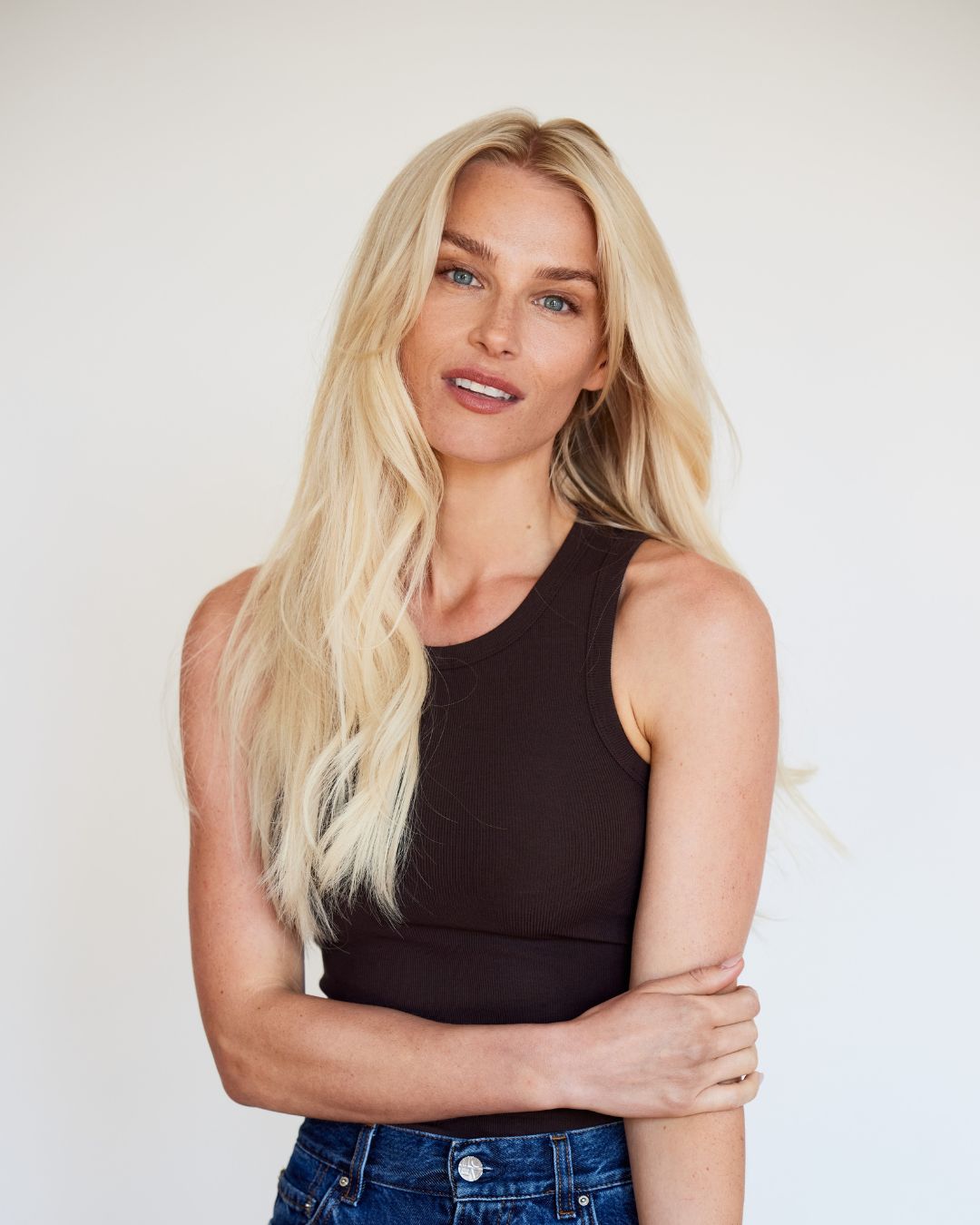 Model with long, blonde BHBD Weft extensions styled straight, wearing a black tank top. 100% Remy hair, gentle extensions.