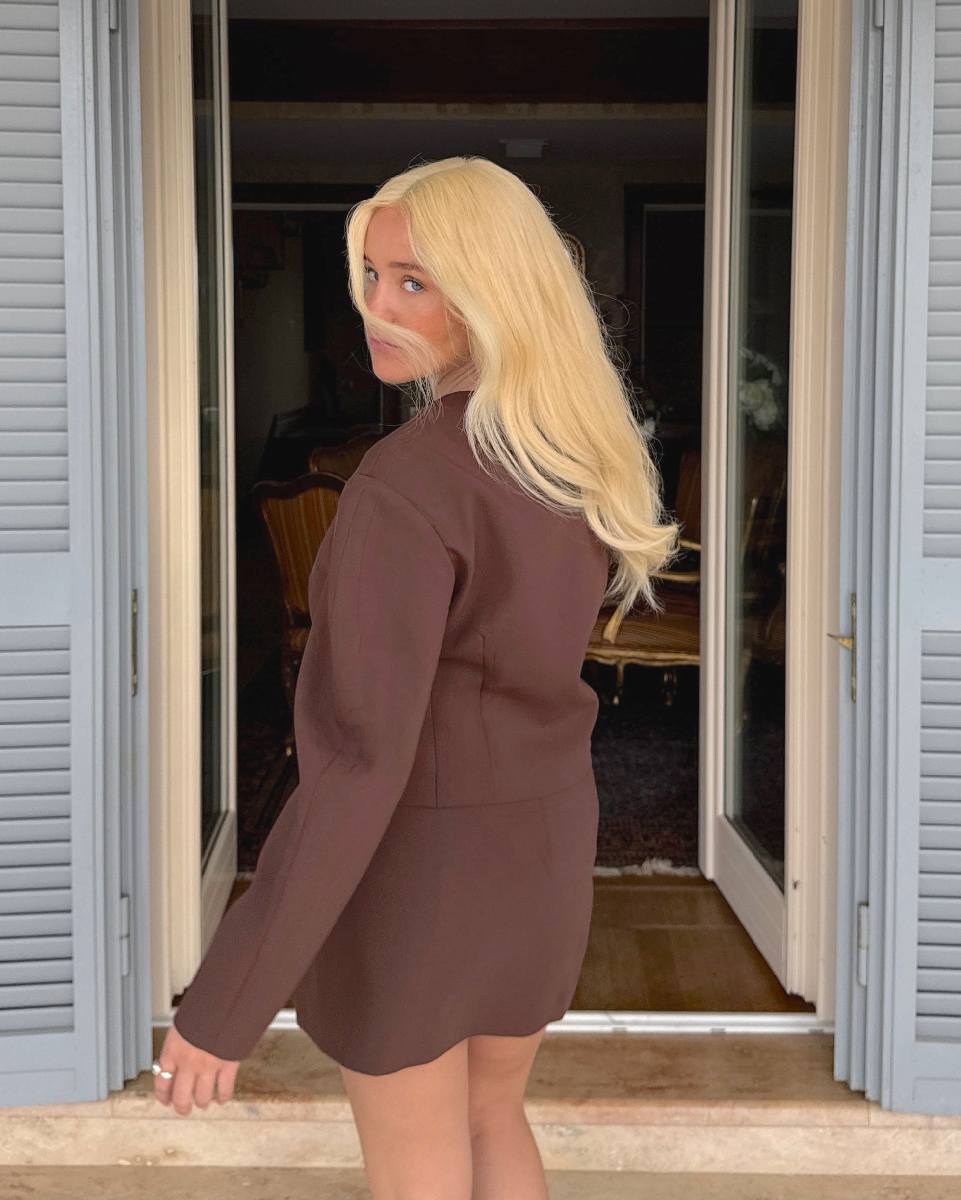 Model outdoor lifestyle shot with Livia Wig – 40cm warm blonde lace wig worn outdoors; natural layered styling with soft waves.