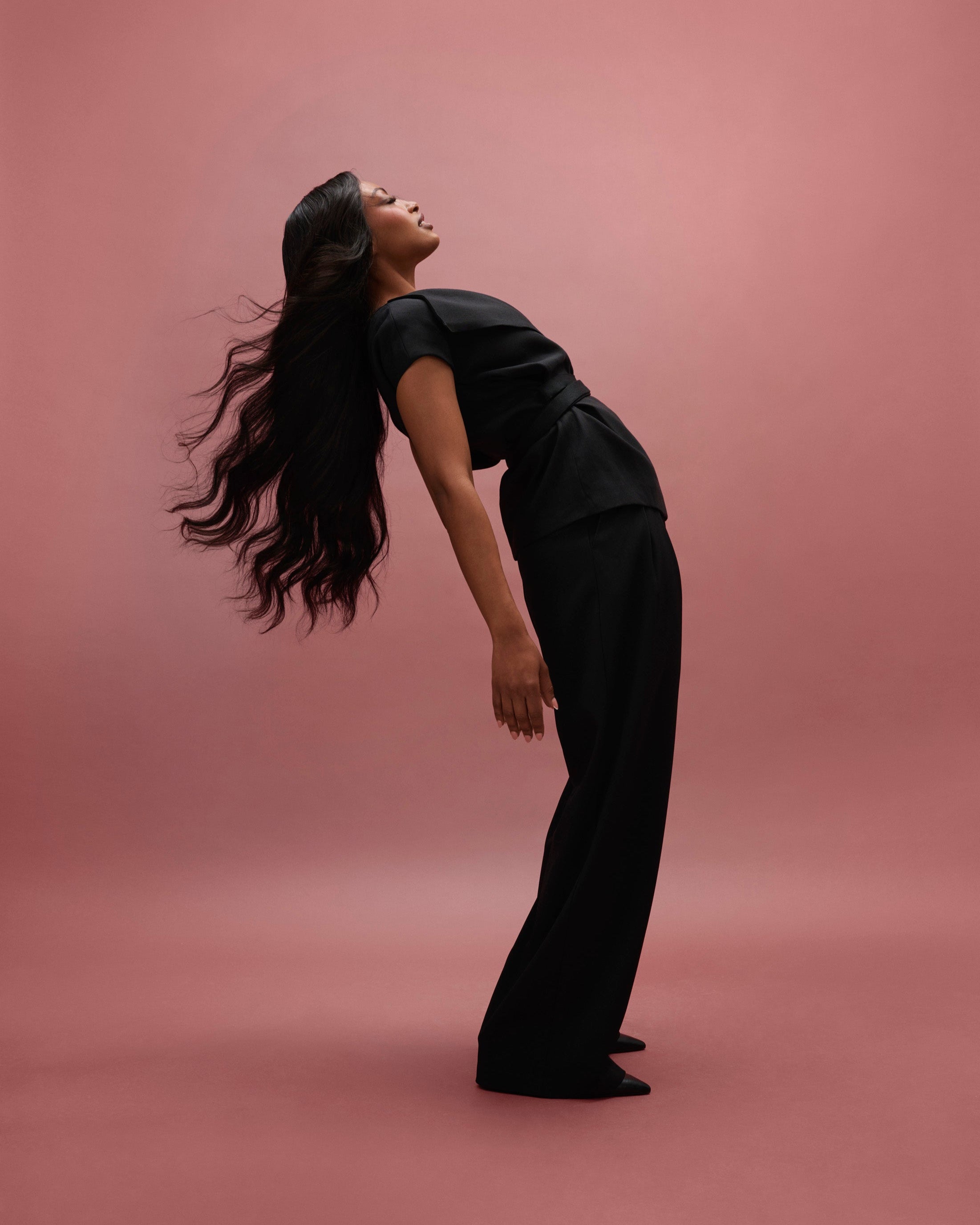 Aurora Wavy Wig 65 cm – deep natural brown human hair wig with subtle warmth and softly permed beach waves in a 65 cm length, featuring HD lace with pre‑plucked hairline and bleached knots, shown on a model leaning back against a pink background