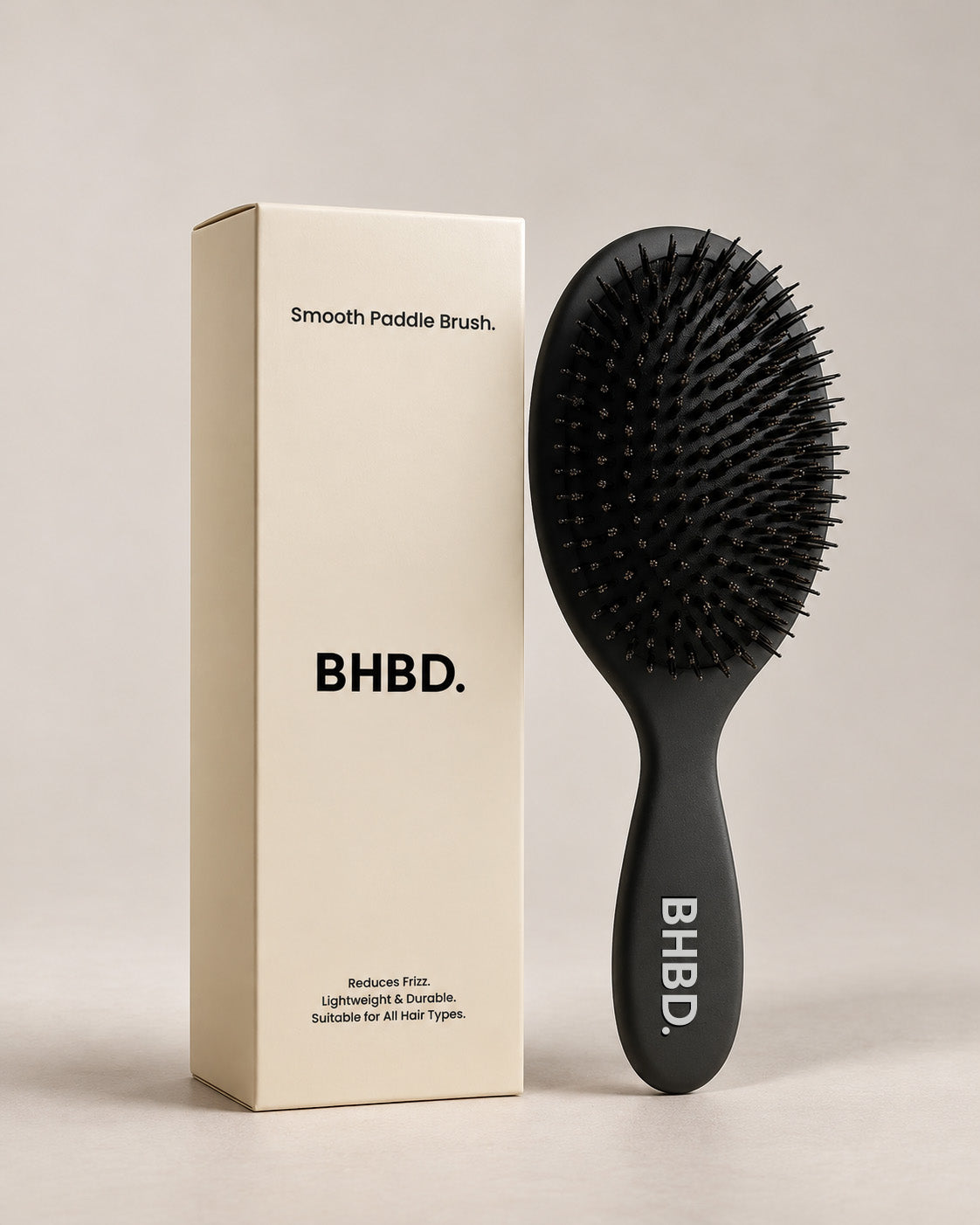 BHBD Paddle Brush – black paddle hairbrush with natural boar and nylon bristles that smooths and detangles hair, shown next to its beige packaging