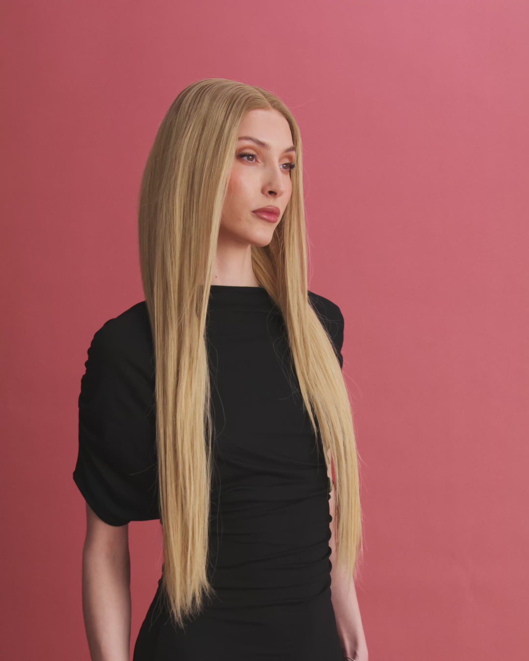 Vera Wig / 65cm – 65 cm light blonde Remy human hair wig with subtle golden tones and darker roots, softly layered, shown in motion on a model against a pink background.