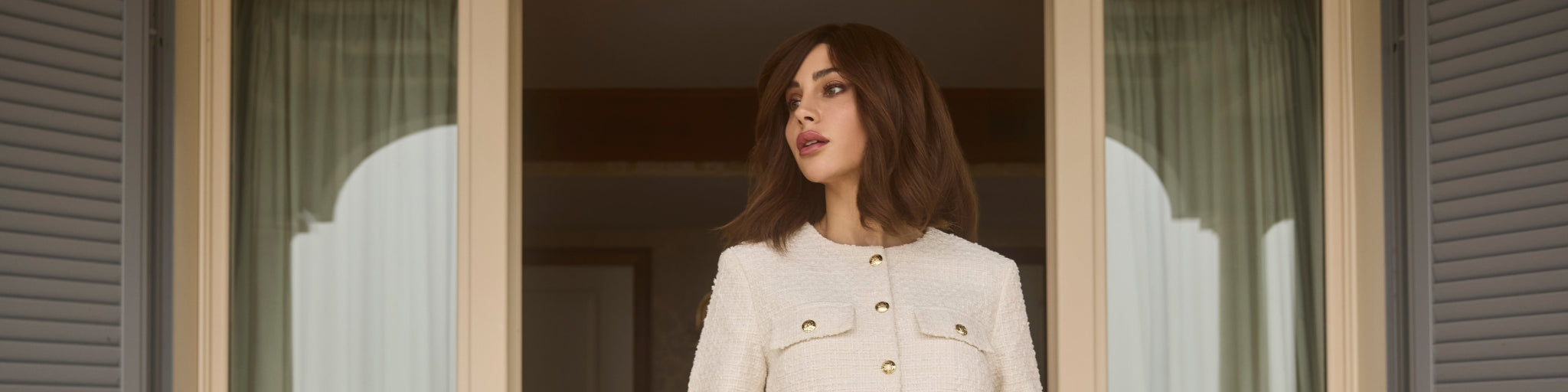 Model wearing a luxurious wig from BHBD’s ‘The Italian Dream’ collection, featuring a natural, seamless look with soft, elegant waves. The model stands confidently in front of an open doorway, embodying timeless Italian sophistication.