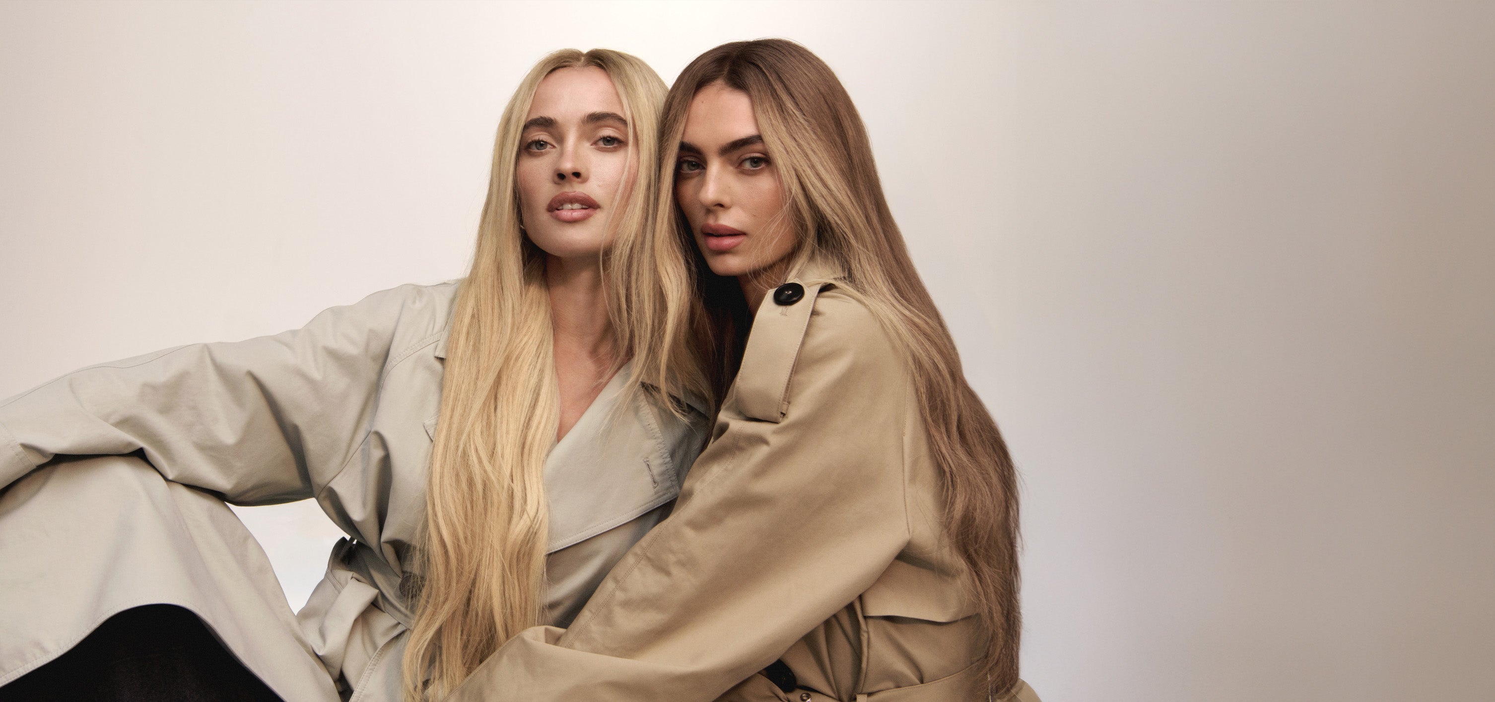 Two women wearing BHBD wigs. One with a long blond wig and one with a dark blond wig