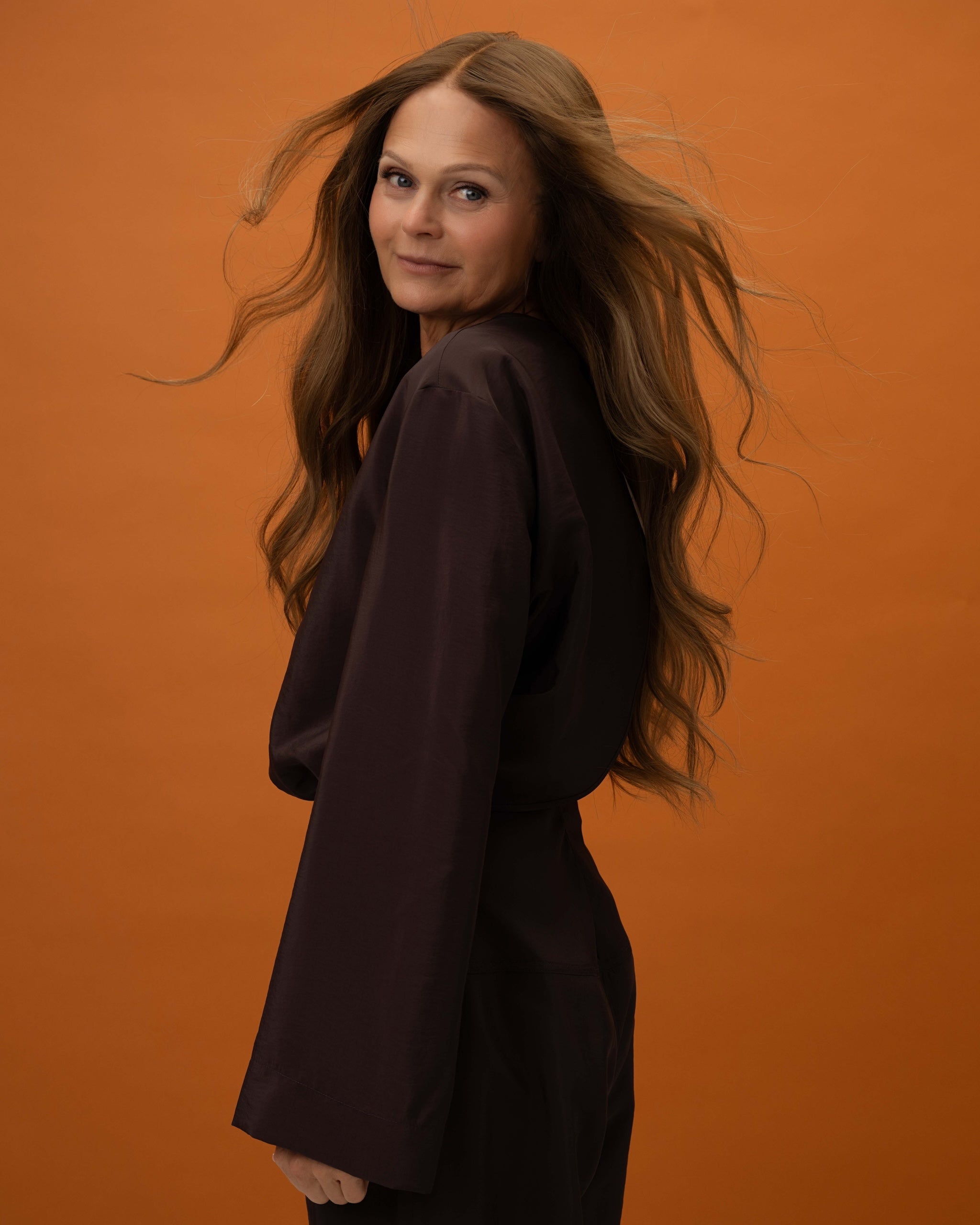 Model side pose with Elena Wig – 50cm full lace wig in caramel brown to medium brown balayage; styled with natural layers.