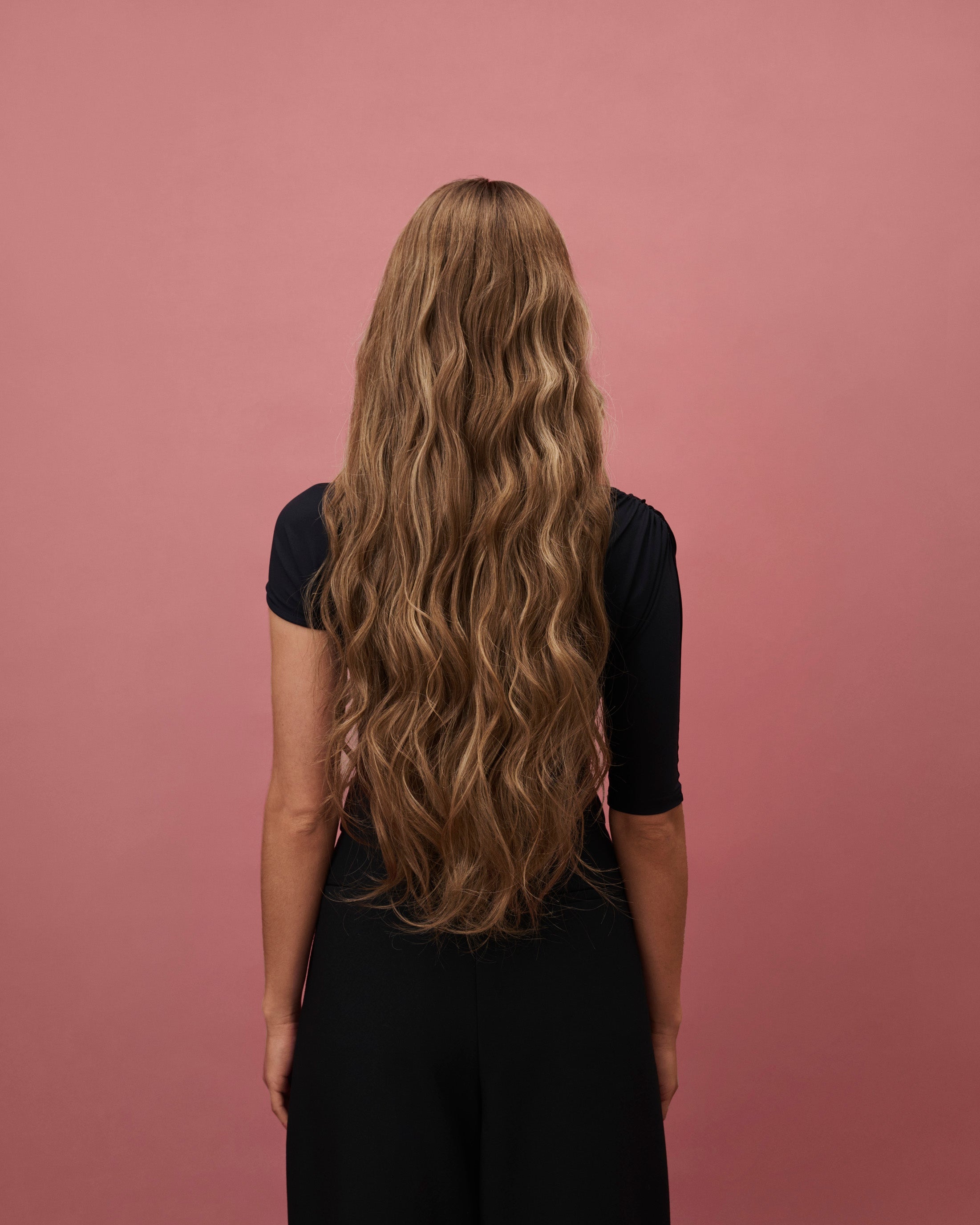 Noble Nightshade Wig 65 cm – dark blonde rooted Remy human hair wig with softly layered 65 cm lengths and money‑piece highlights on HD lace, shown on a model from the back.