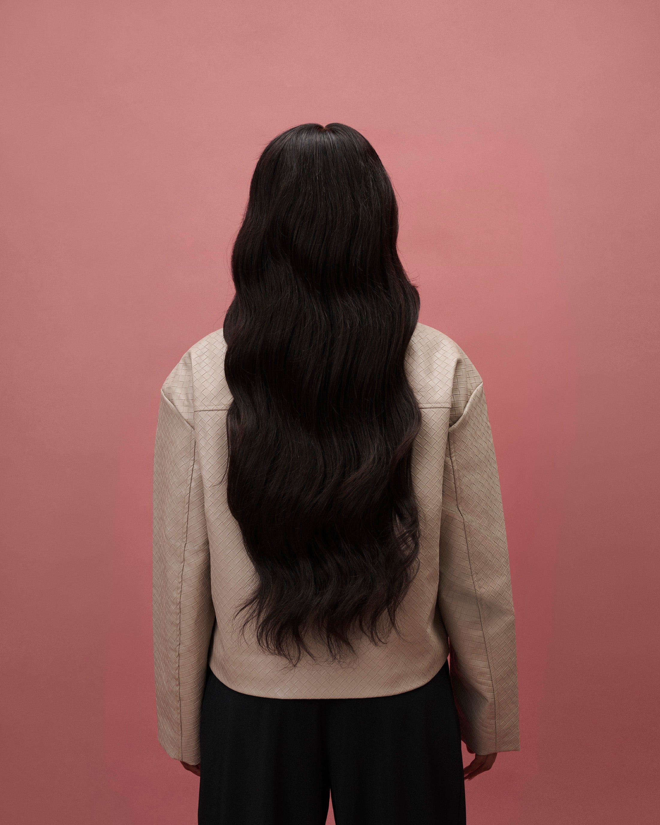 Back view of Aurora Wavy Wig 65 cm – dark brown Remy human hair with soft beach waves on HD lace, worn by a model in a beige jacket and black pants