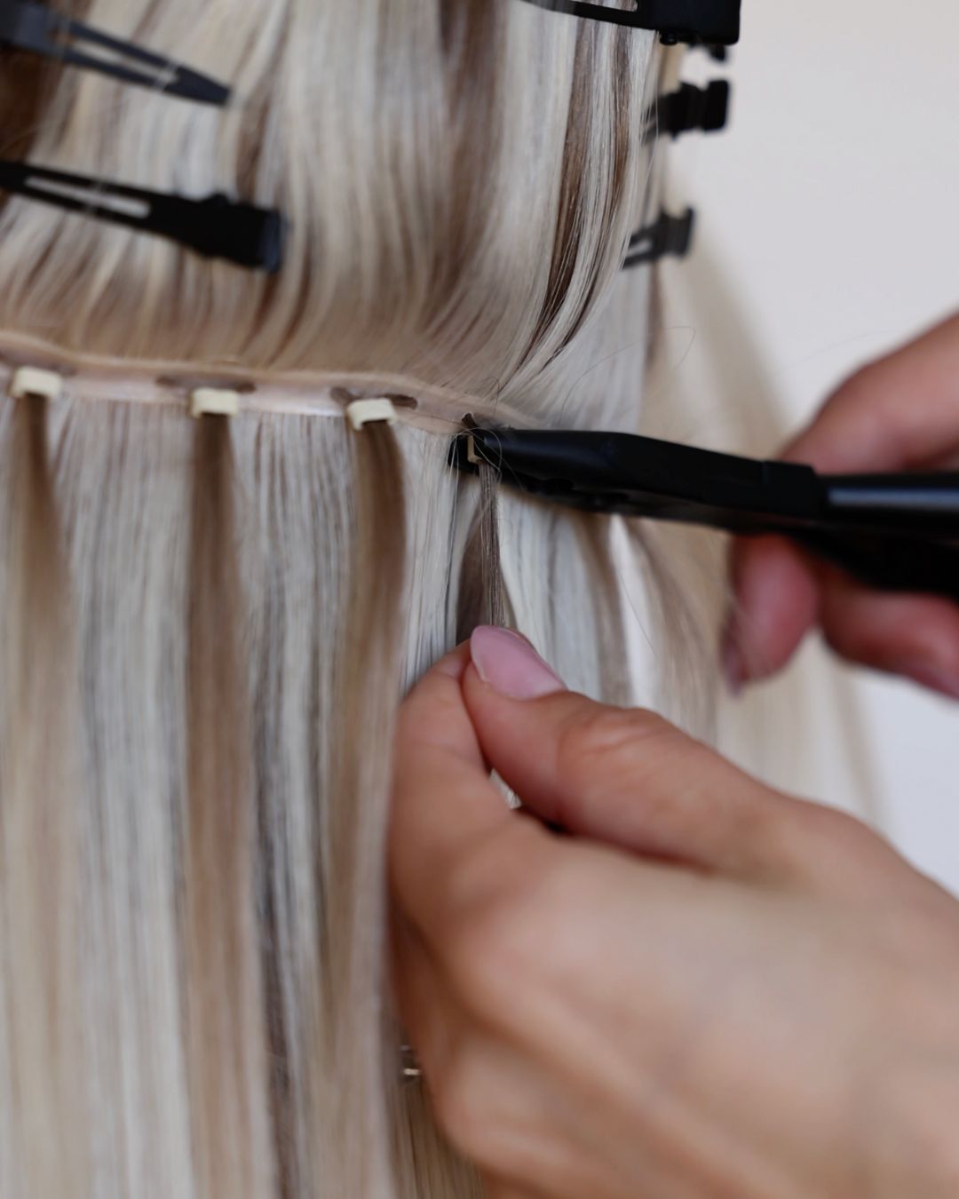Close-up of stylist using pliers to secure BHBD Weft extensions with micro rings. 100% Remy hair, gentle extensions.