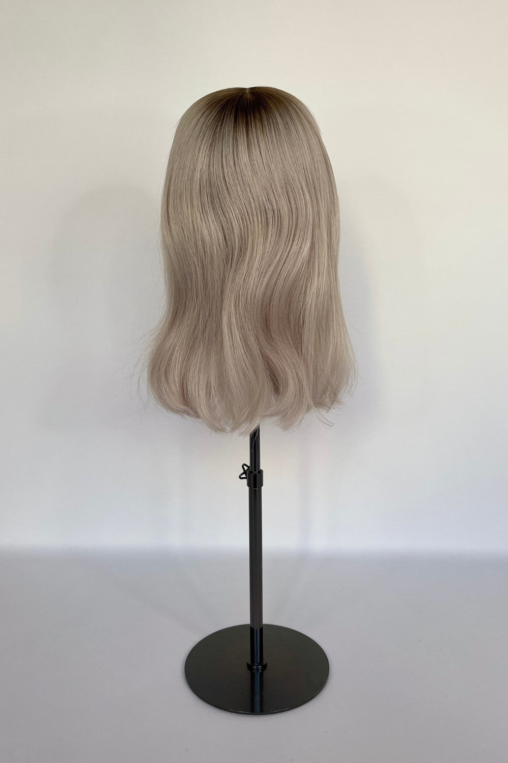 BHBD premium half or full lace wig in an ash blonde shade with darker blond roots and soft, smooth waves, displayed on a mannequin stand. Made with 100% real Remy hair, featuring a natural parting and seamless finish for an elegant and realistic look.