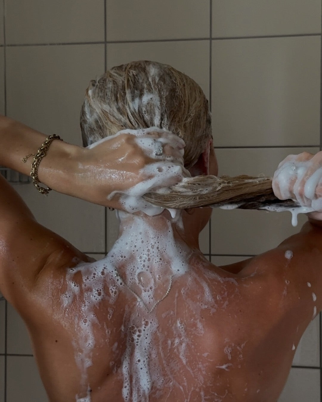Person washing hair with BHBD shampoo, showing product use in a bathroom setting.